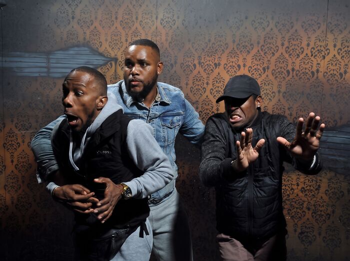 Three men with hilarious scared expressions in a haunted house photo.