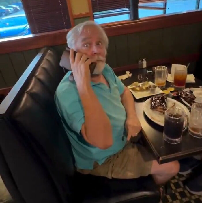 An older man from the Karen couple calls police on restaurant manager using his phone at a booth. An older man from the Karen couple calls police on restaurant manager using his phone at a booth.