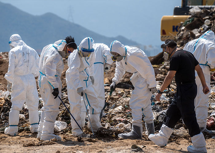 People in hazmat suits investigating debris in outdoor area People in hazmat suits investigating debris in outdoor area