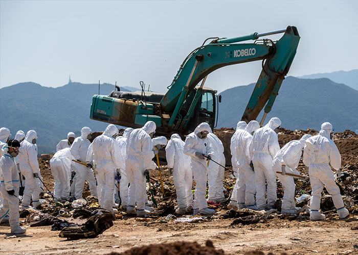 Group of people in hazmat suits working near excavator on dirt site Group of people in hazmat suits working near excavator on dirt site
