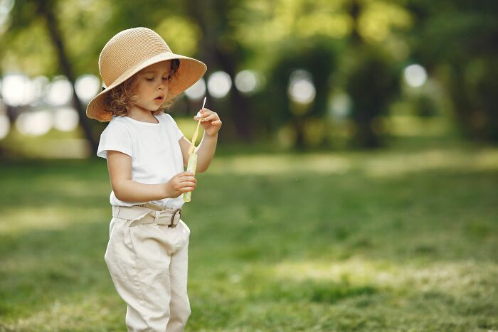 A young child in a sunhat blowing bubbles, sharing innocent secrets in a park