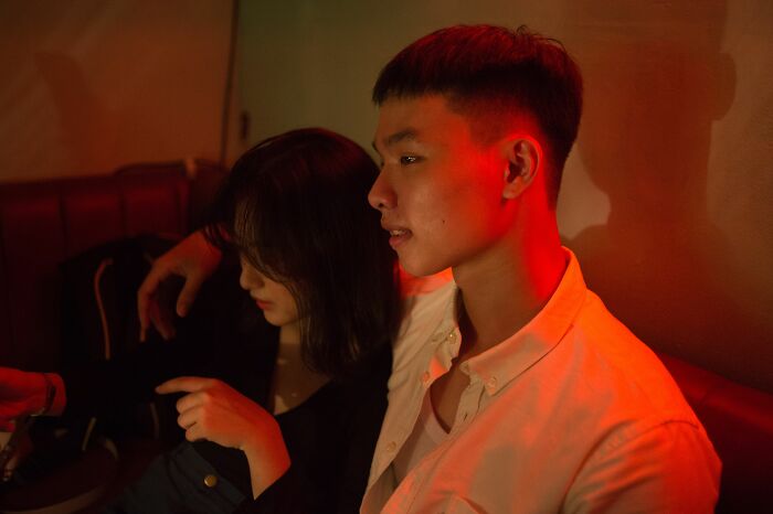 A young couple sitting closely together under red ambient lighting while sharing secrets