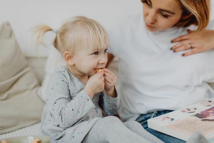 A mother and her young daughter share a quiet moment, as if telling secrets while snacking