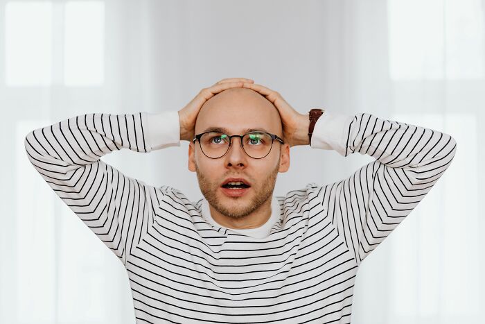 Surprised bald man with glasses holding head, discovering secrets online