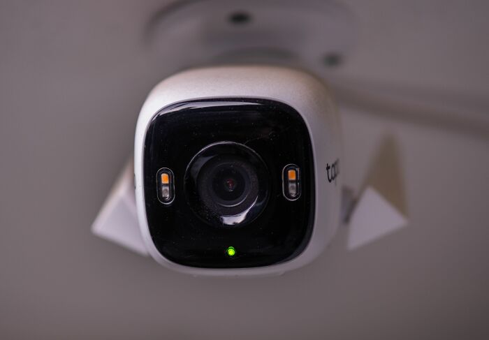A white security camera mounted on a ceiling captures secrets with its lens
