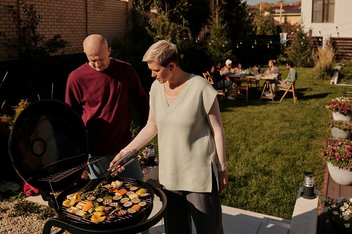 A couple grilling vegetables during a backyard gathering, sharing secrets by accident