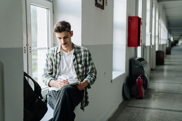 Young man writing in notebook while sitting on hallway window, linked to family feuds.