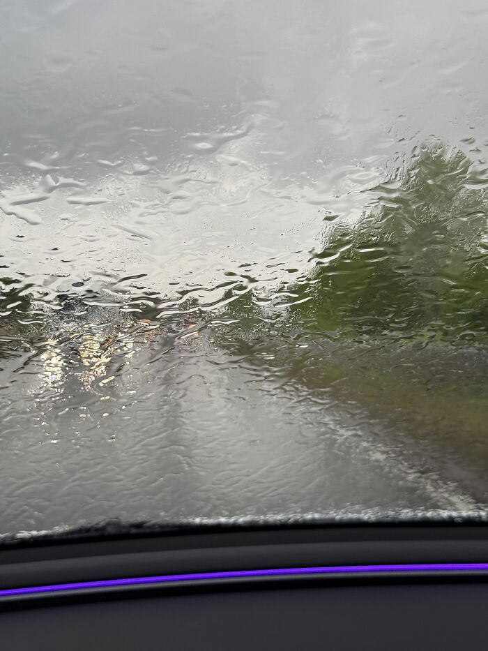 Raindrops covering a car windshield, presenting an absurd moment during rainy weather.