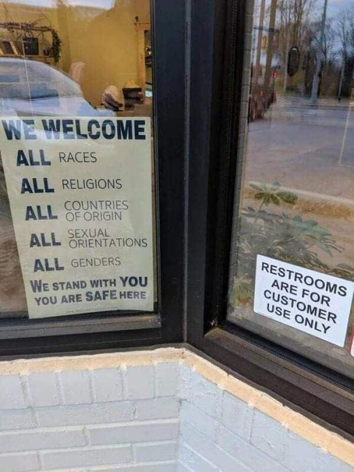 Juxtaposed signs for welcoming all people but limiting restrooms to customers, showing modern life in America dynamics.