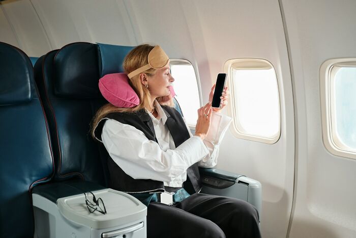 A woman wearing a sleep mask using her phone to get better seats on flights