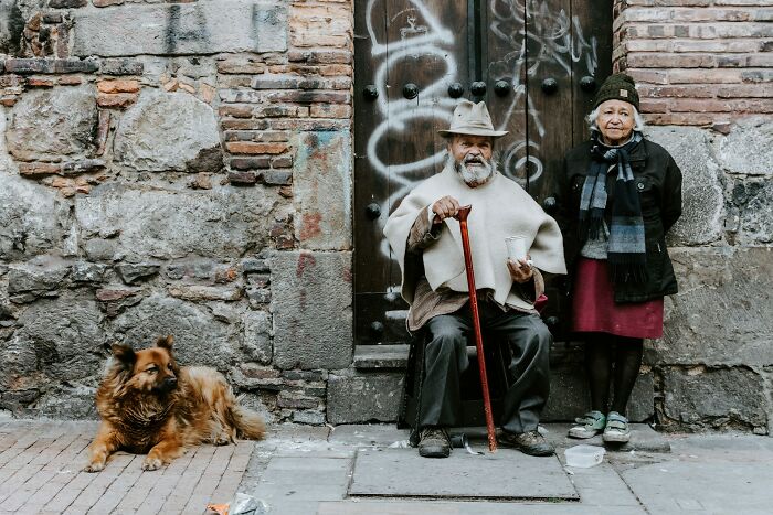 Elderly couple sitting outside with a dog on a weathered stone street corner