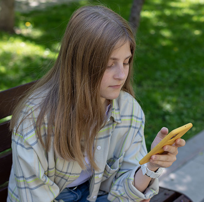 Teen girl looking at phone outdoors, concerned expression Teen girl looking at phone outdoors, concerned expression