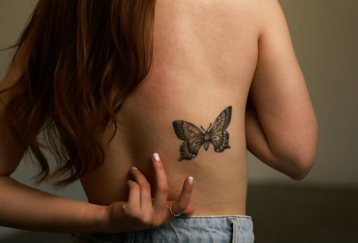 Woman showing a butterfly tattoo on her back, highlighting unique partner stories and intelligence questions.
