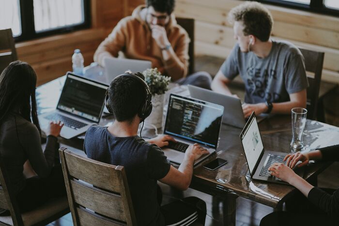 Group of colleagues working on laptops around a table, depicting tech industry insiders at work.