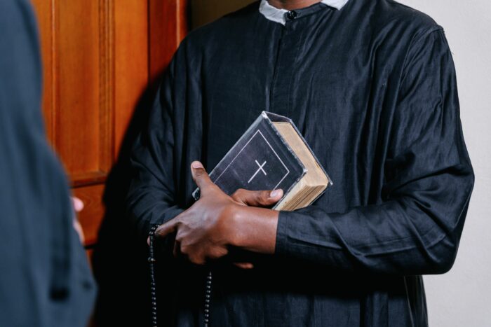 Pastor holding Bible and rosary beads in church setting