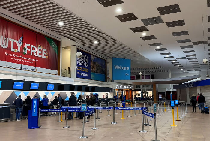 Empty airline check-in desks and queuing lanes inside an airport terminal, related to airport gate change.