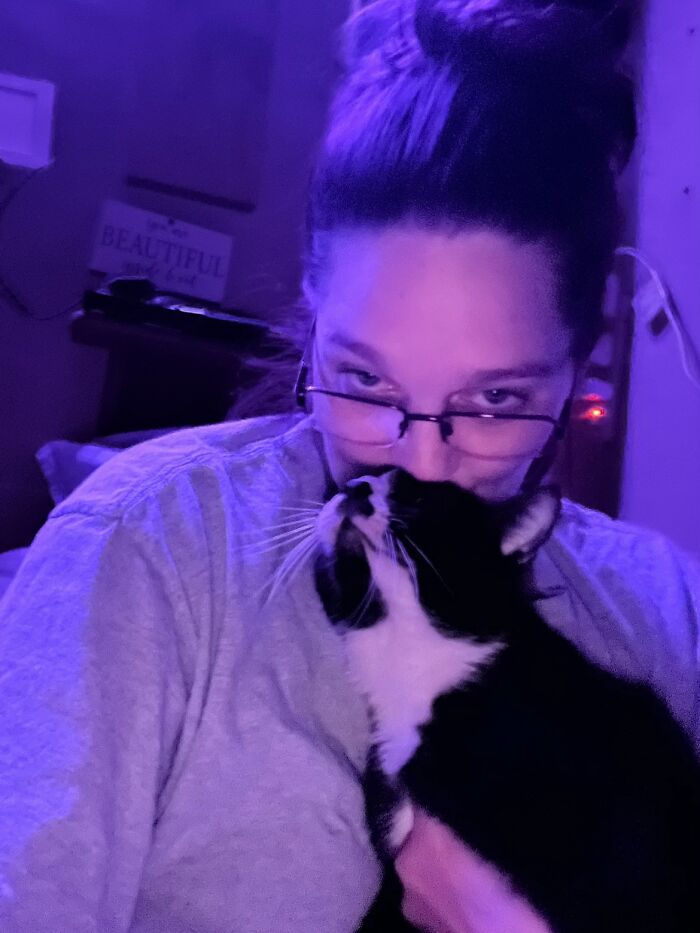 A woman with glasses cuddling her black and white tuxedo cat, sharing life stories with pets