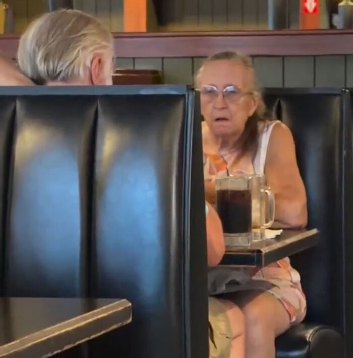 Elderly woman looking distressed at a restaurant booth during an argument with restaurant manager. Elderly woman looking distressed at a restaurant booth during an argument with restaurant manager.