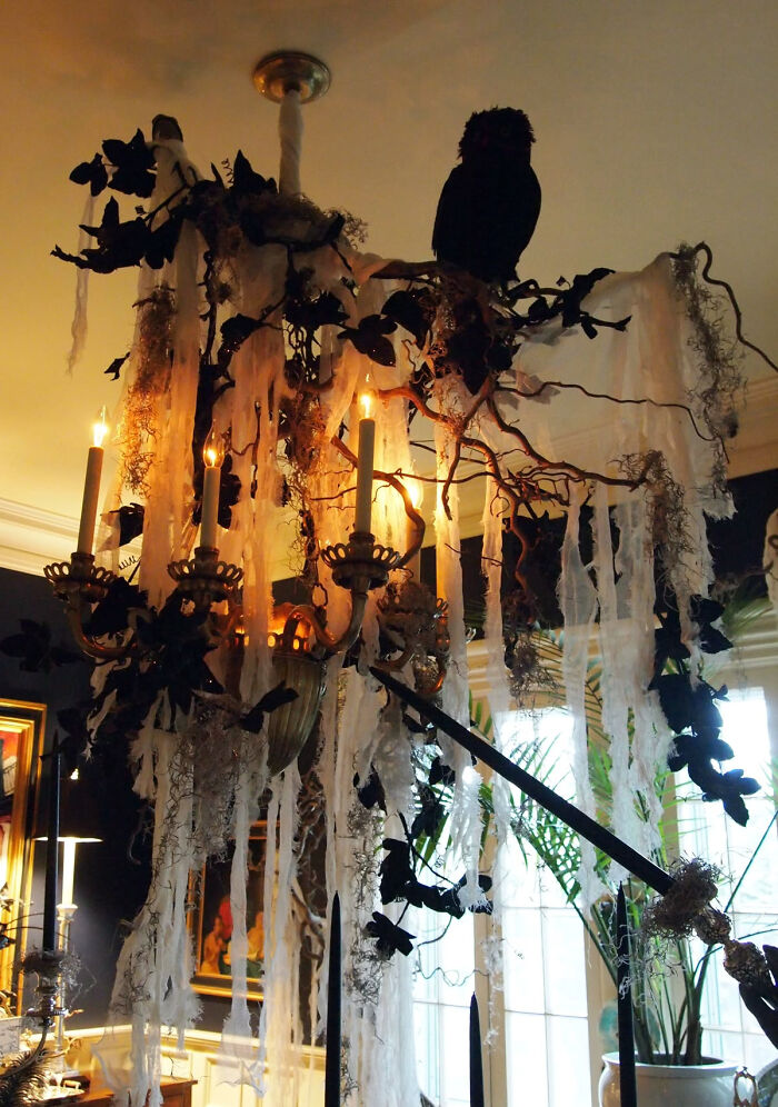 Chandelier decorated with fake cobwebs and black birds for Halloween home inspiration.