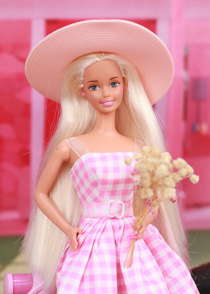 Blonde Barbie doll wearing a pink gingham dress and wide hat amid Barbie packaging outrage.