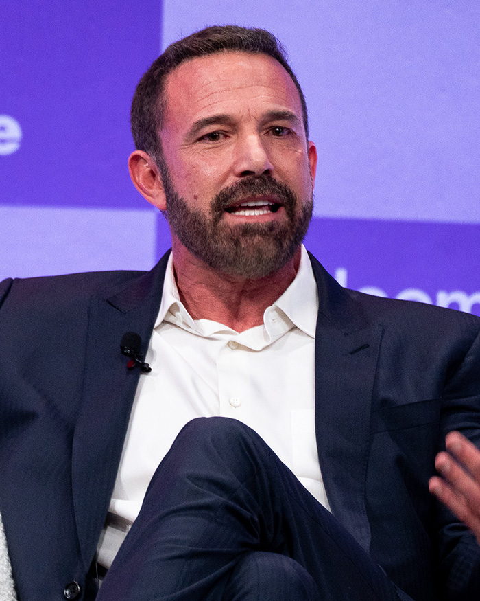 Ben Affleck speaking at event wearing white shirt and dark suit