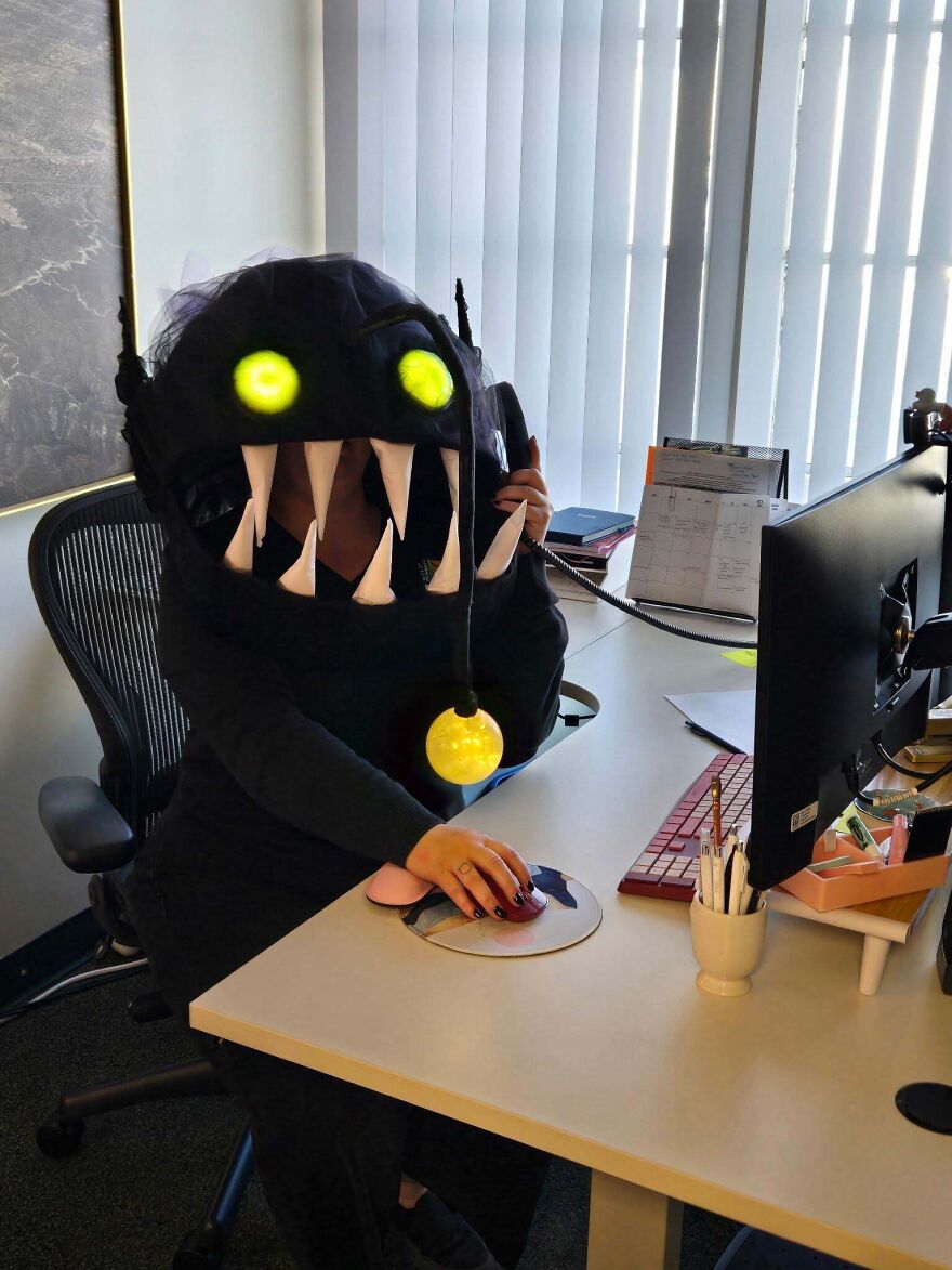 Woman sitting at a desk wearing a glowing anglerfish mask as a creative Halloween costume.