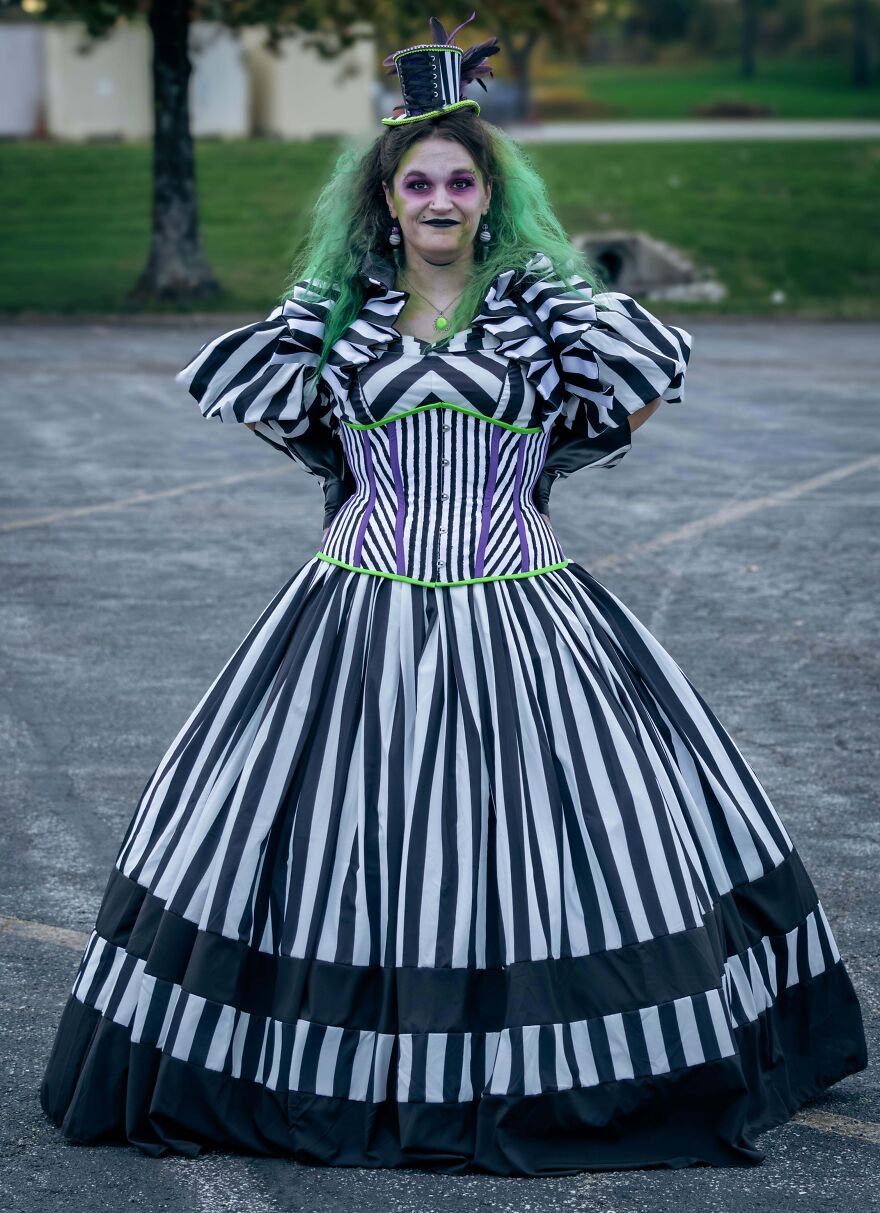 Woman in a detailed black and white striped gown and green hair presenting her Halloween costume.