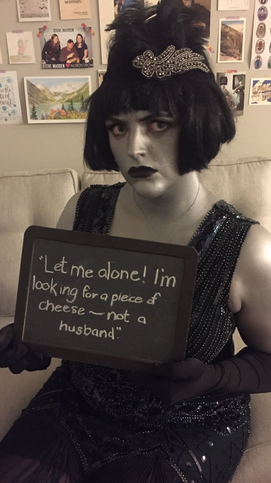Woman in grayscale flapper Halloween costume holding a chalkboard sign looking for a piece of cheese