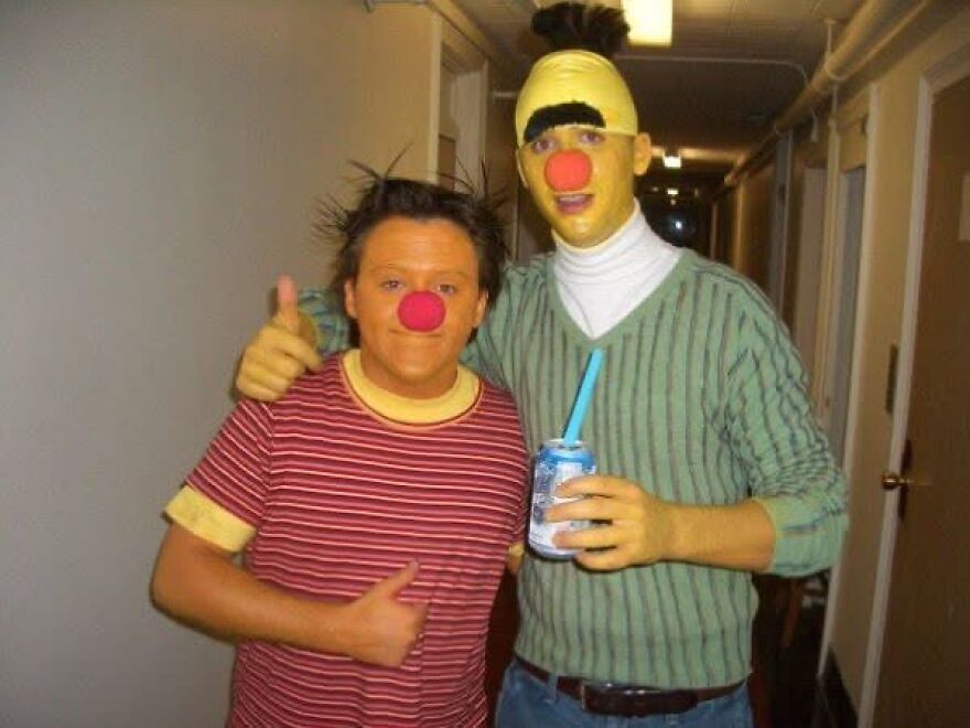 Two friends posing in creative Bert and Ernie Halloween costumes with face paint and wigs.