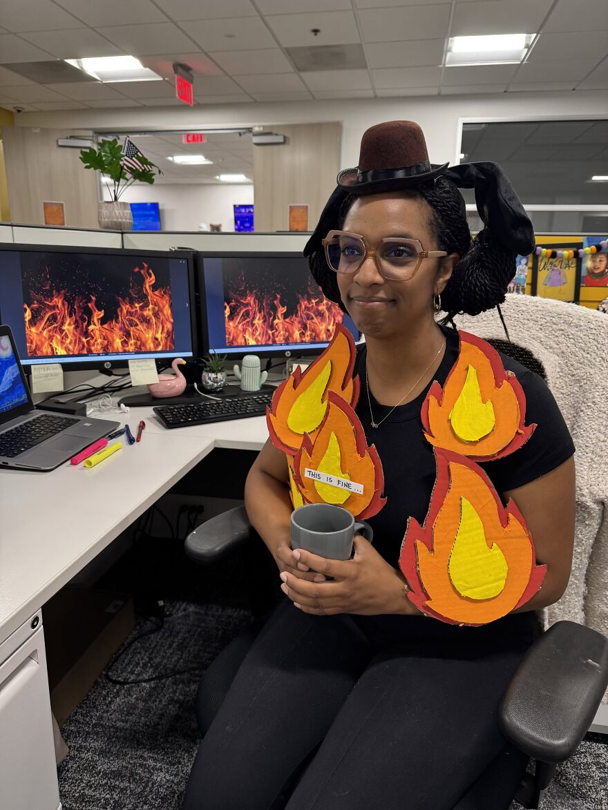 A woman wearing a creative fire meme Halloween costume holding a mug at an office desk.