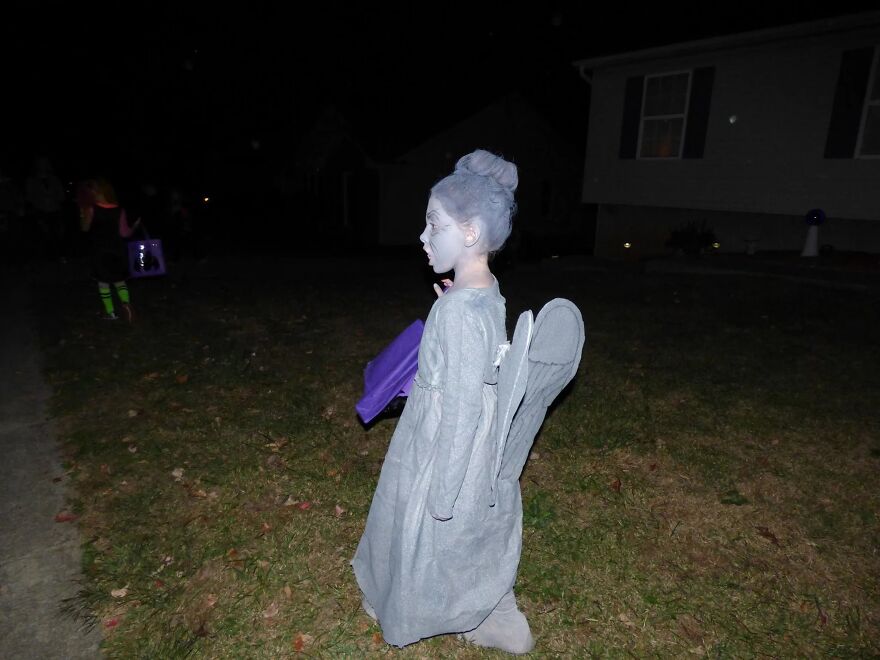 A young child dressed as a weeping statue in an impressive Halloween costume outdoors at night