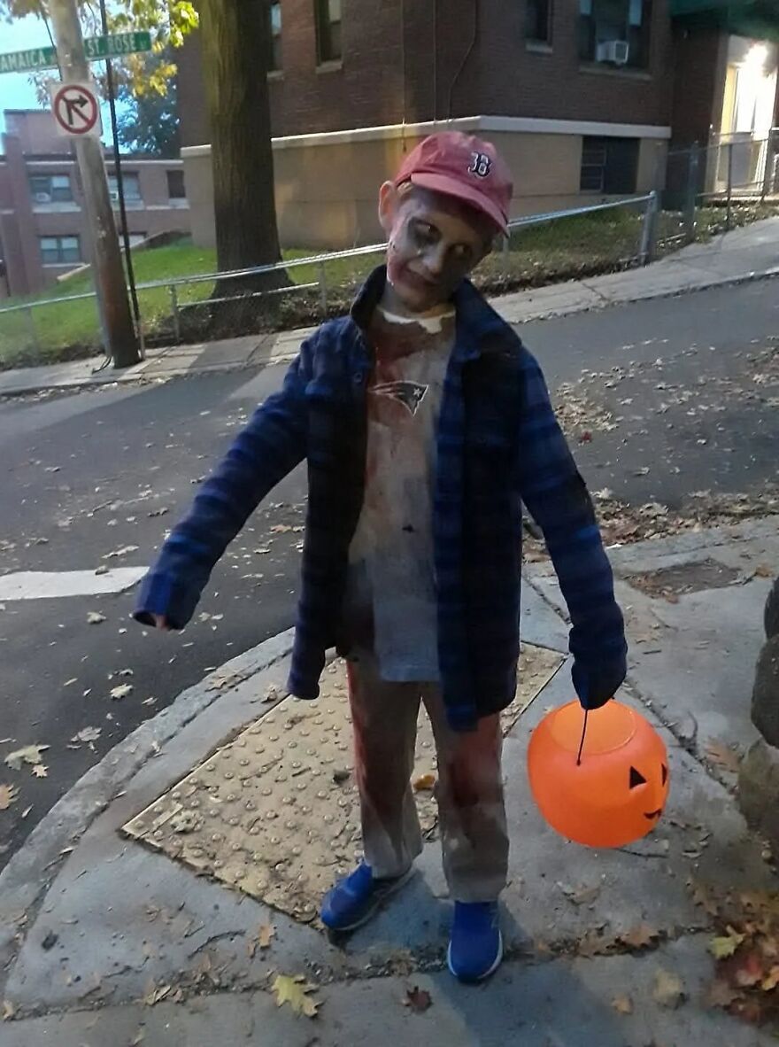 A kid in a creepy zombie outfit holding a pumpkin bucket for Halloween costumes