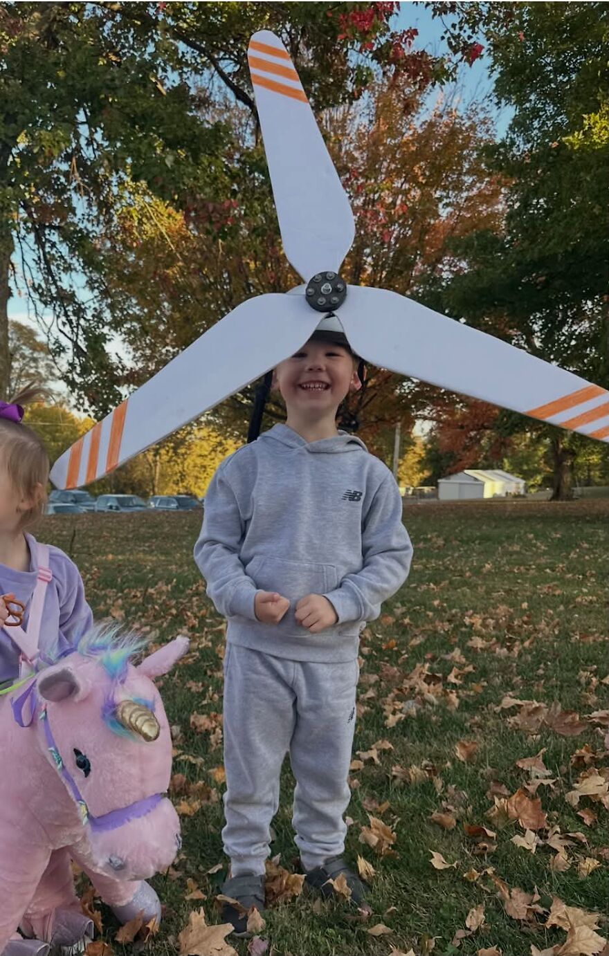 A young boy wearing a giant wind turbine prop on his head as a unique Halloween costume outdoors.
