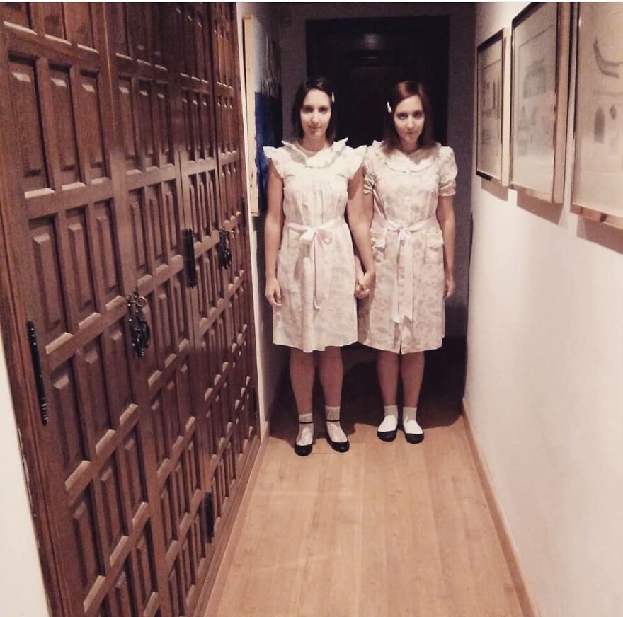 Two women dressed up in spooky creepy twin dresses as creative Halloween costumes in a hallway.