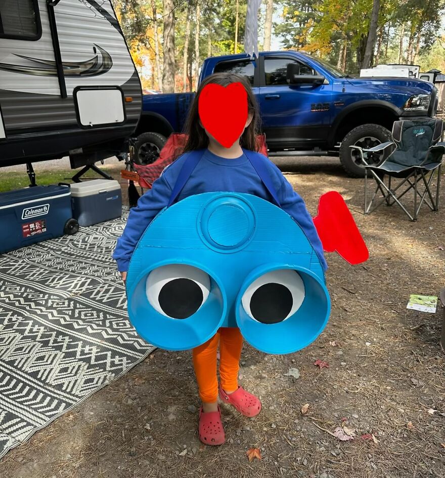 Child wearing a creative homemade view-master toy Halloween costumes while standing outdoors near a campsite.