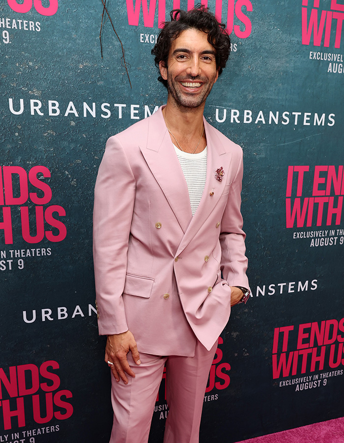 Justin Baldoni smiling in a light pink suit on the red carpet following celebrity texts news. Justin Baldoni smiling in a light pink suit on the red carpet following celebrity texts news.