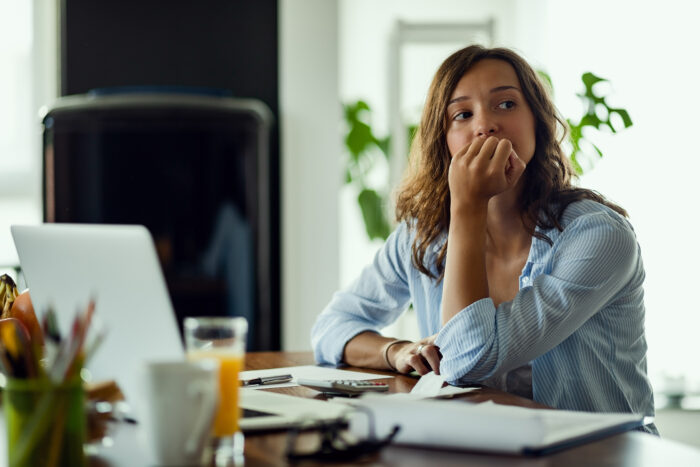 Worried woman sitting at a table with a laptop, looking anxious while using a flight tracker for an imaginary flight.