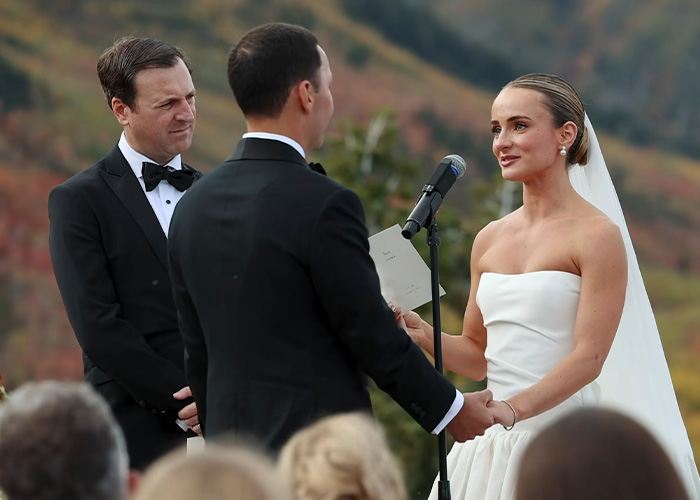 A bride reading her controversial wedding vows into a microphone in front of her groom.