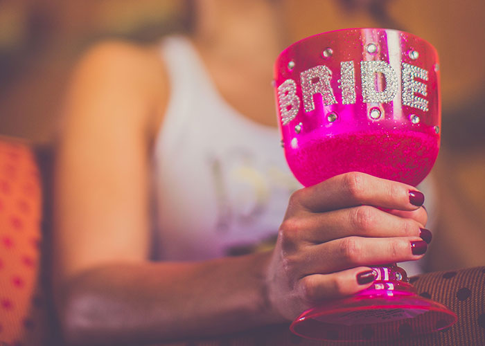 A woman holding a pink glittery cup with BRIDE written on it during a bachelorette party.