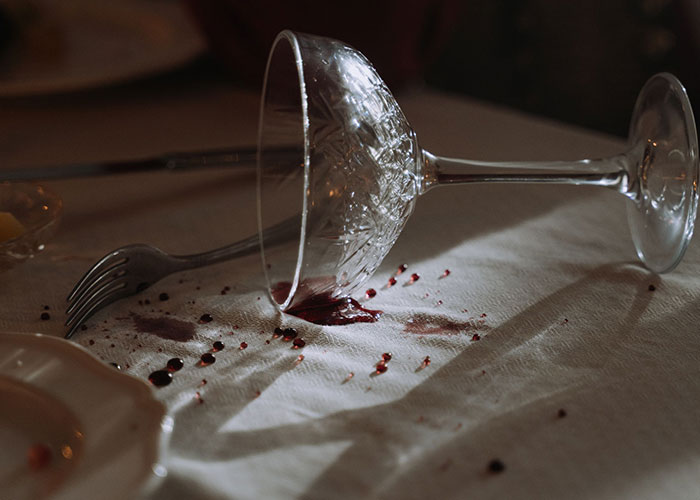 An overturned glass with red wine spilled on a white tablecloth, symbolizing bridezilla chaos.