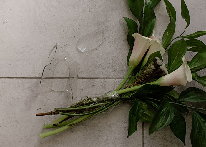 White calla lily flowers lying next to shattered glass on a stone floor, symbolizing how a bridezilla ruins hotel rooms