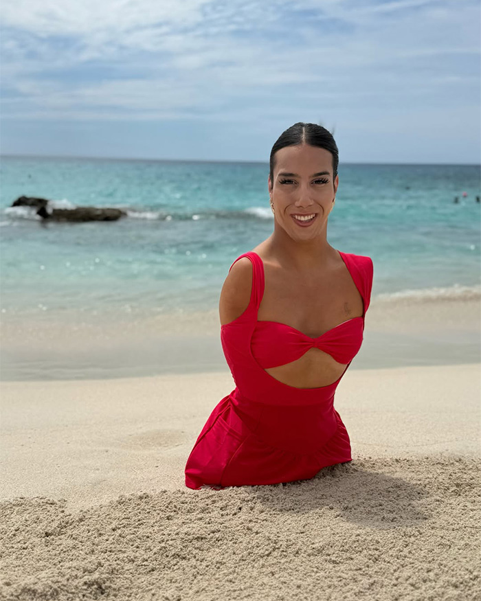Trans influencer born without limbs smiles on the beach in a red swimsuit. Trans influencer born without limbs smiles on the beach in a red swimsuit.