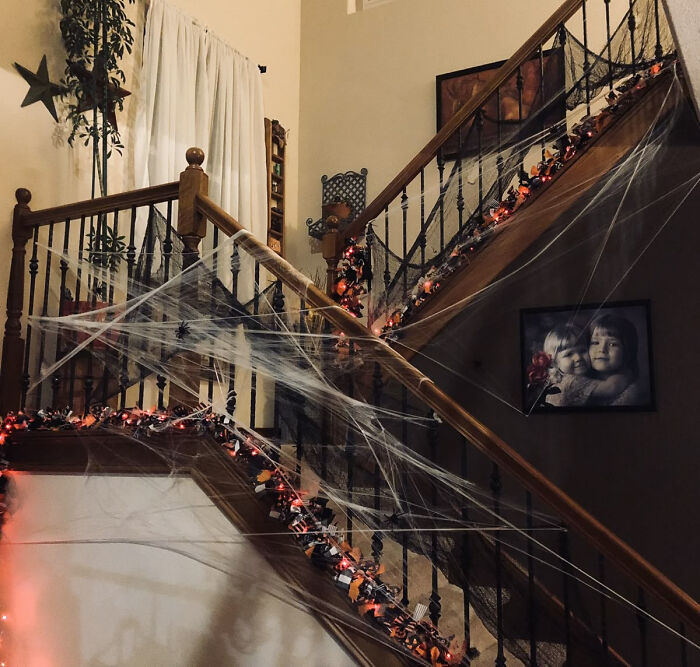 Wooden staircase covered in thick cobwebs and festive orange garlands for Halloween styling.