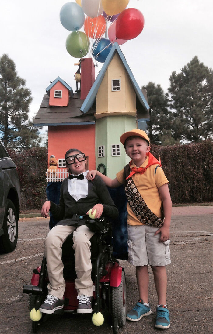 Two kids in movie Up costume, showcasing creative people with disabilities on Halloween with a house wheelchair.
