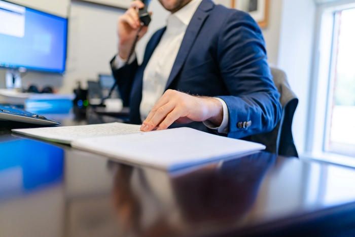 A man in a suit at his desk discussing tree law issues over the phone with documents. A man in a suit at his desk discussing tree law issues over the phone with documents.