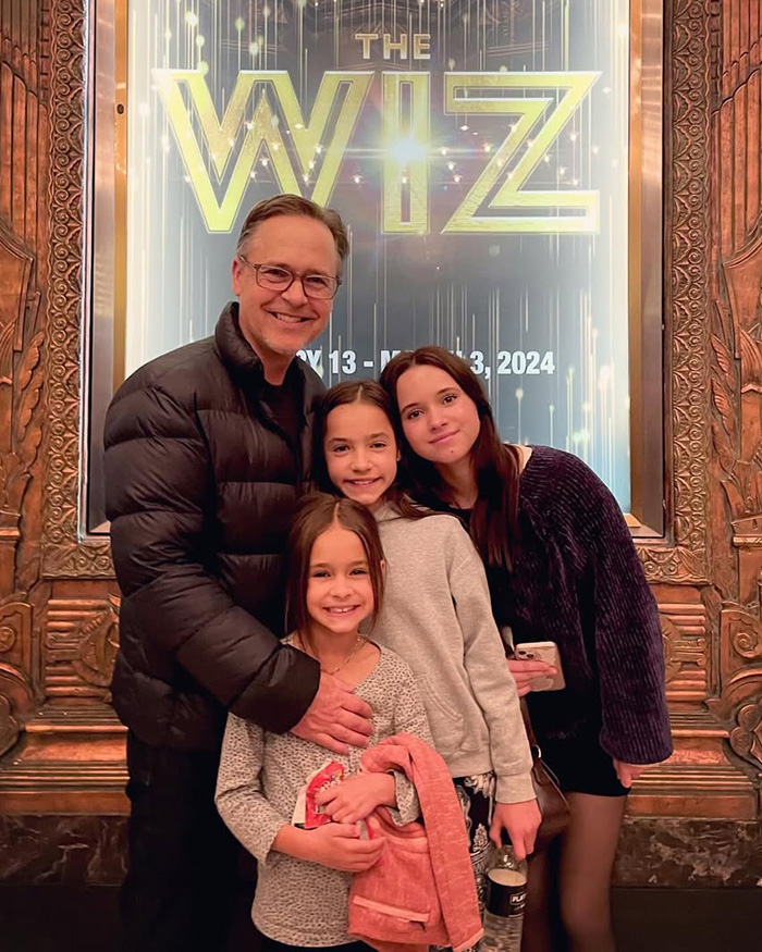 Smiling family of four posing together in front of The Wiz theater sign