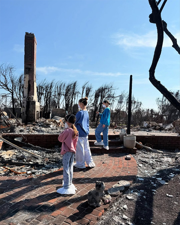 Children wearing masks walk through the ash and ruins of a burned home, reflecting Fiona's difficult journey.