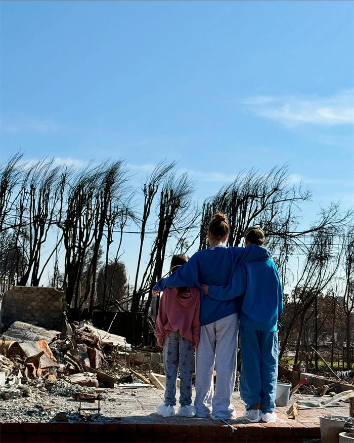 Three girls stand together, backs to the camera, looking at fire destruction, representing Fiona's struggles.