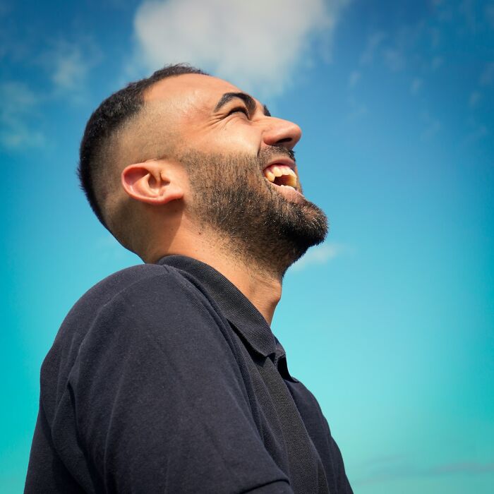 A man laughing against a clear blue sky, evoking painful infidelity stories.
