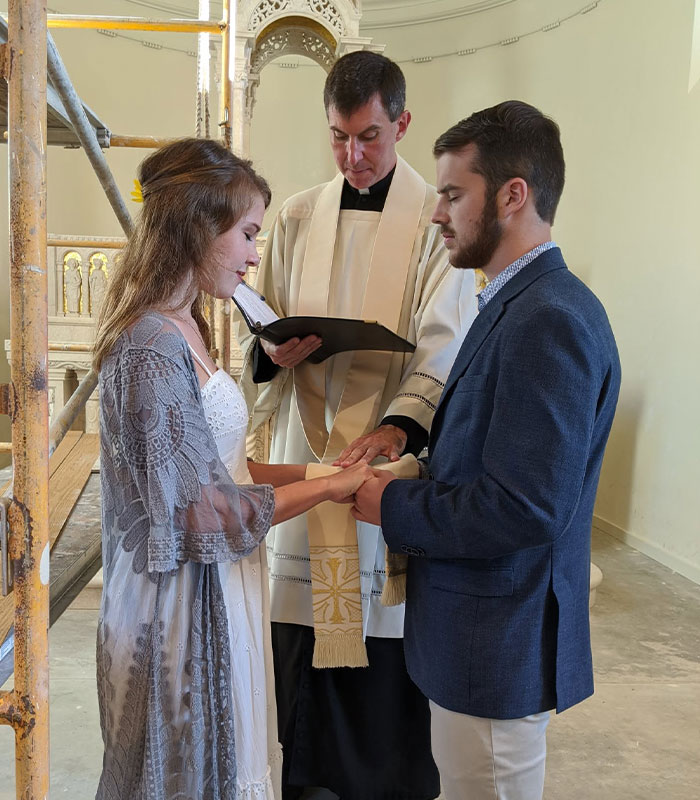A priest performing a ceremony for a young couple holding hands.